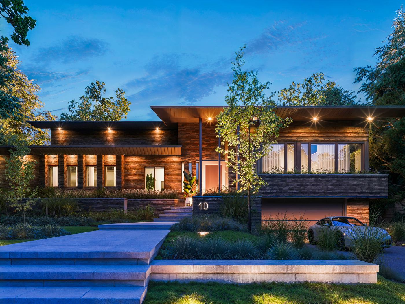 A contemporary Montréal house at dusk, its windows lit, seen from the front walk.